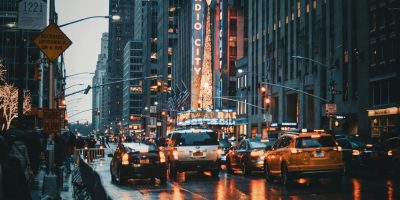 Dramatic city street view of New York's Radio City at night with reflections and taxis.