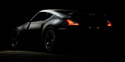 A dramatic shot of a Nissan 370Z sports car illuminated in darkness with vibrant tail lights.